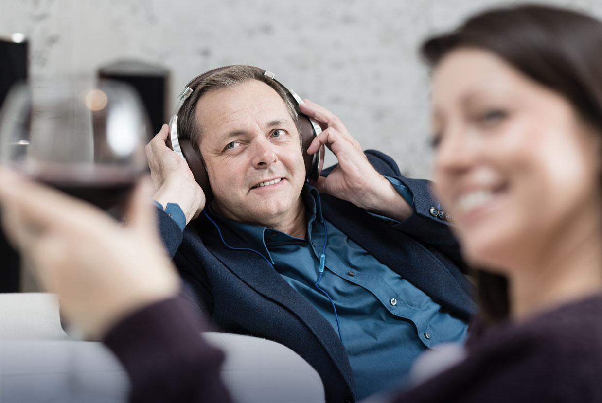 [Translate to 中文:] Man listening to music with head phones. His wife drinks a glas of wine.